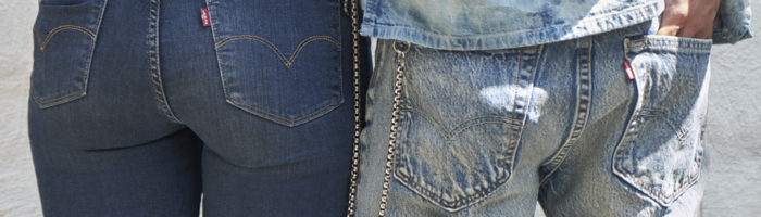 A close up of two people's back pockets. The person on the left has their hands in their back pockets and they wear dark wash Levi's® jeans. The person on the right has their right hand in their right back pocket and they wear light acid wash Levi's® jeans with a silver chain hanging on their left side.