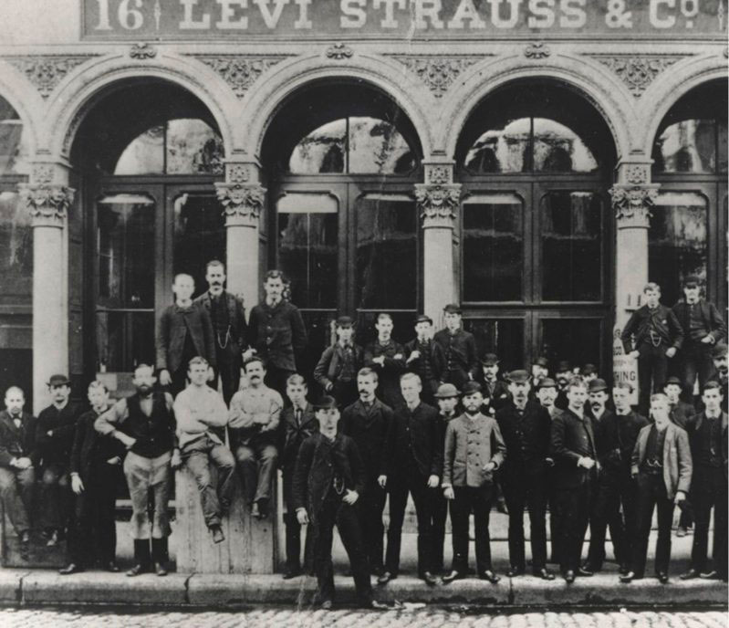 a black and white photo of employees standing in front of one of the original Levi Strauss & Co. buildings.