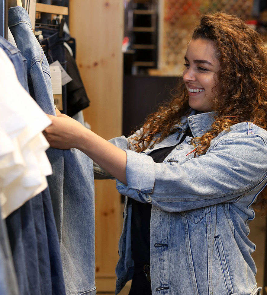 woman wearing a trucker jacket looking at a rack of jeans