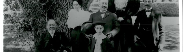 An old black and white image of a family posing in front of a large oak tree.
