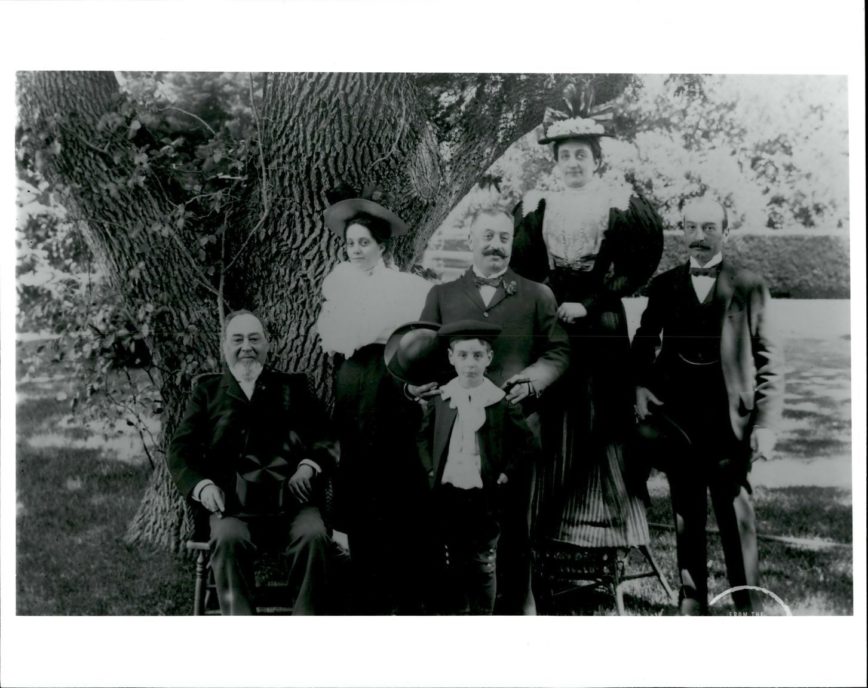 An old black and white image of a family posing in front of a large oak tree.