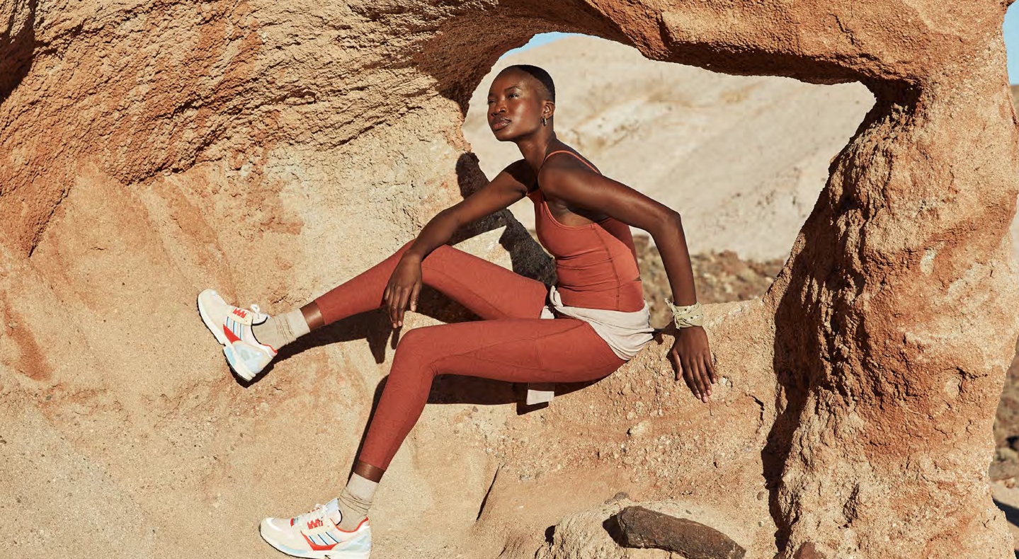 A person sits on an outdoor rock formation wearing a Beyond Yoga® set in a brick color