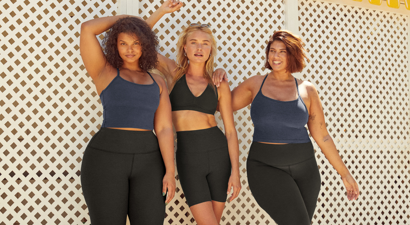 Three people lean against a white wall wearing Beyond Yoga® products