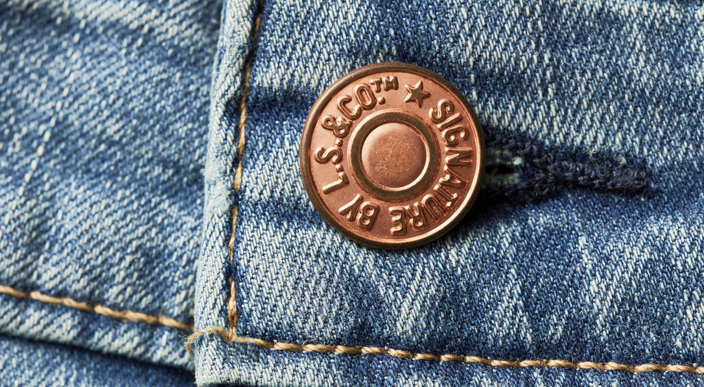 A close up of a copper rivet button reading Signature by LS&Co.