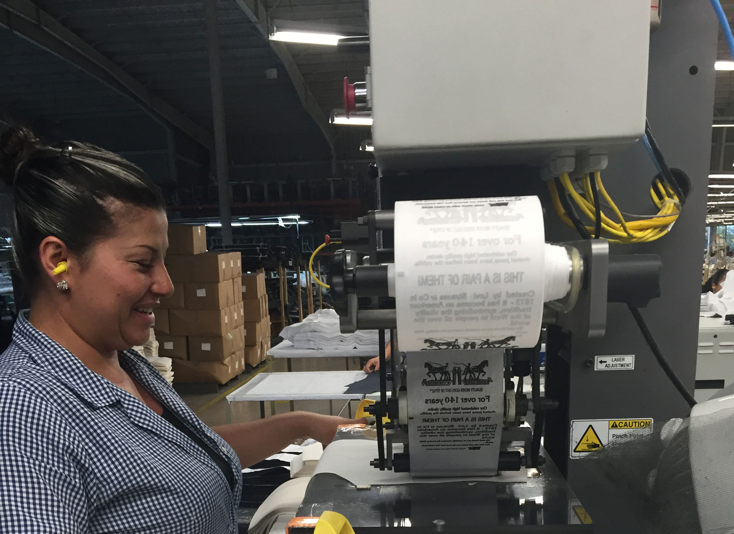 A person smiles sitting at a desk working a large label maker machine