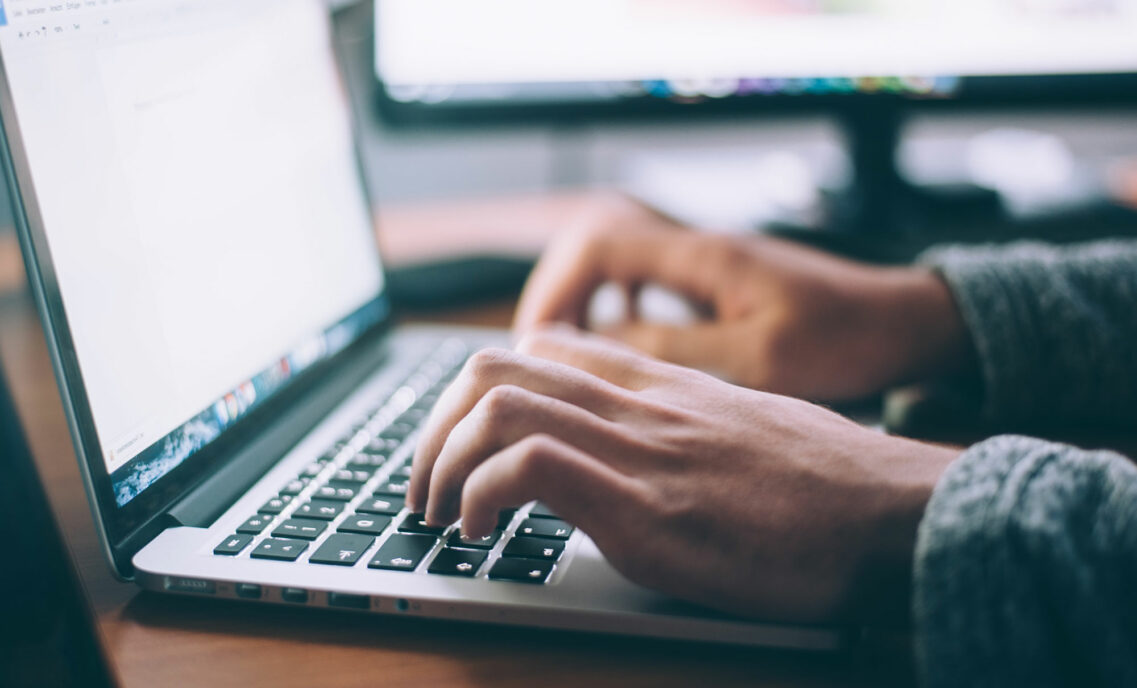 hands typing on an Apple laptop keyboard