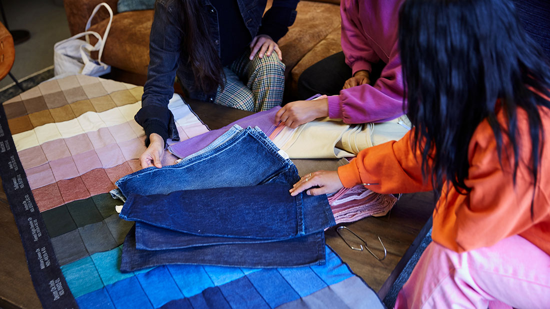 three pairs of hands rifle through a stack of denim samples sitting on a grid of fabric samples