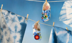 The new tie-dye Croc from the Levi's® x Crocs collection hang on a clothesline with clothespins, against a blue background.