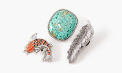 A close-up of three Crocs Jibbitz® from Levi's®. From left to right: an orange koi fish Jibbitz®, a turquoise stone Jibbitz®, a metalic silver feather Jibbitz®
