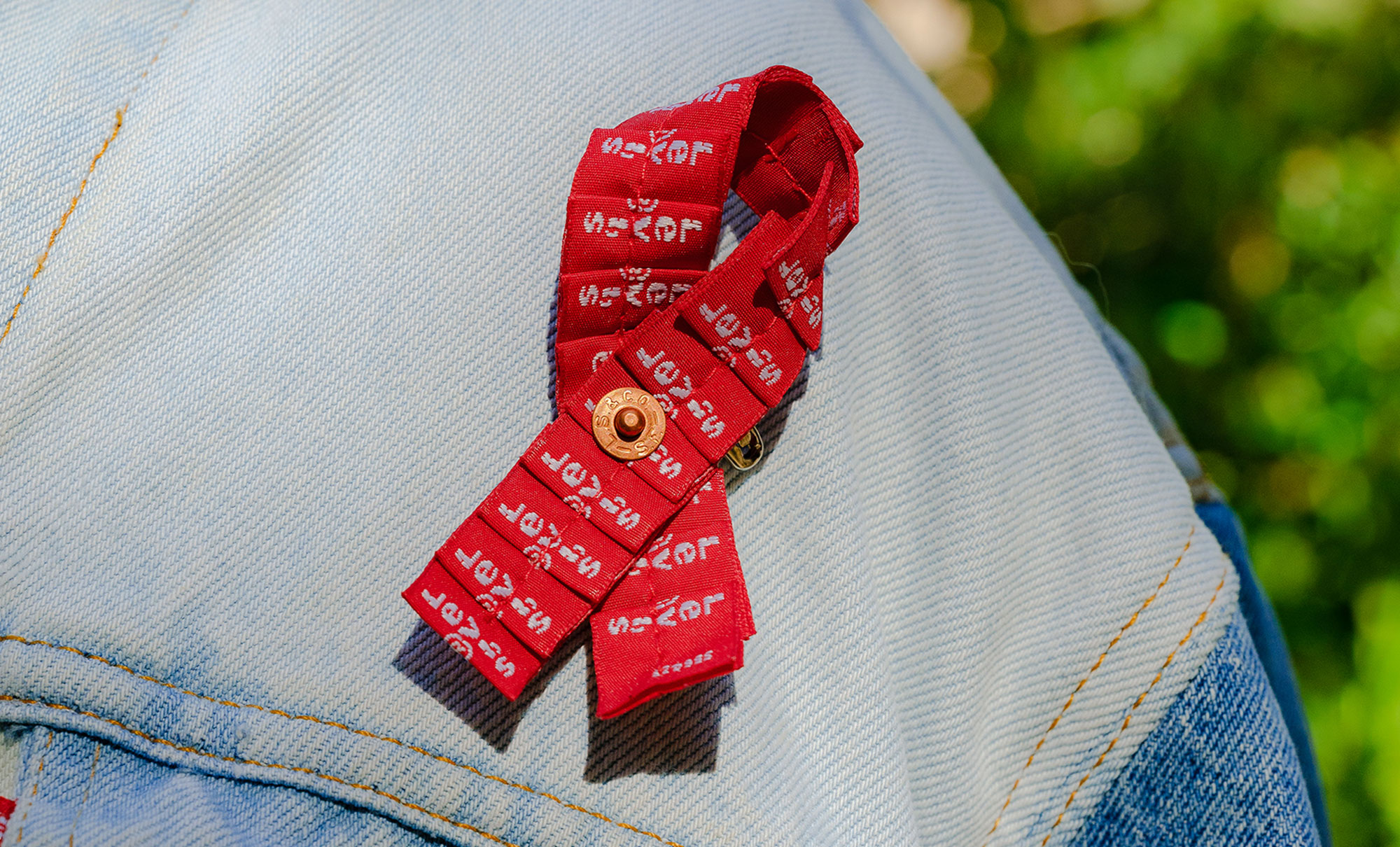 A close up of a red ribbon made of Levi's® red tabs on a light wash denim jacket.The red ribbon is the universal symbol of awareness and support for people living with HIV.