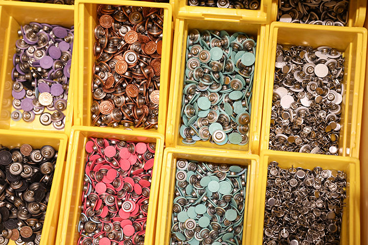 An overhead shot of Levi's® jeans buttons separated by color into yellow plastic containers.