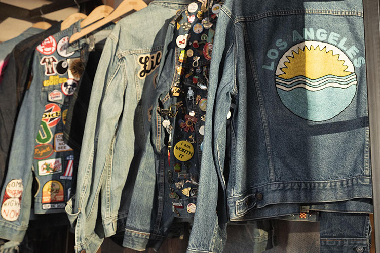 Levi's® denim jackets hang on a clothes rack with the back facing the audience. The jackets have various patches and designs on the denim.