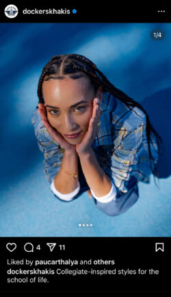 A screenshot of a Dockers® Instagram post. The photo is taken at an above angle of a woman with her hands in her chin. She has long black braids and is wearing a blue flannel against a blue background. Caption reads "Collegiate-inspired styles for the school of life. Shop now @ dockers.com"