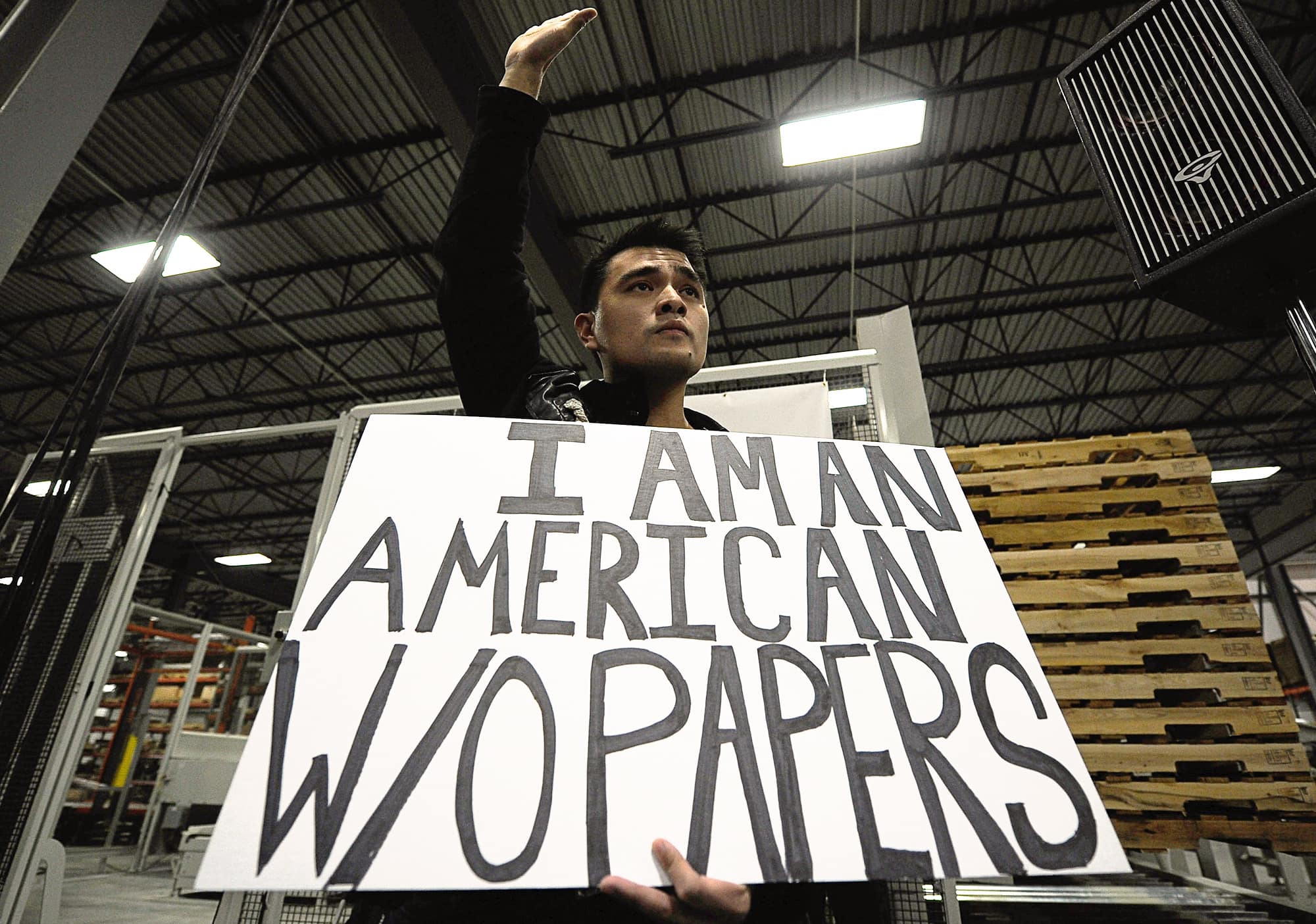 A person raises their right hand and holds a sign that reads