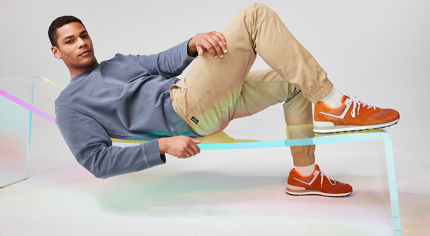 A person lays down on a see-through fluorescent bench. They have cropped black hair and are wearin ga long sleeve grey shirt and khaki pants from Denizen For Levi's®. Their left hand is propped against their bent right leg and they are wearing white socks and orange-red sneakers. Photo by Julia Johnson