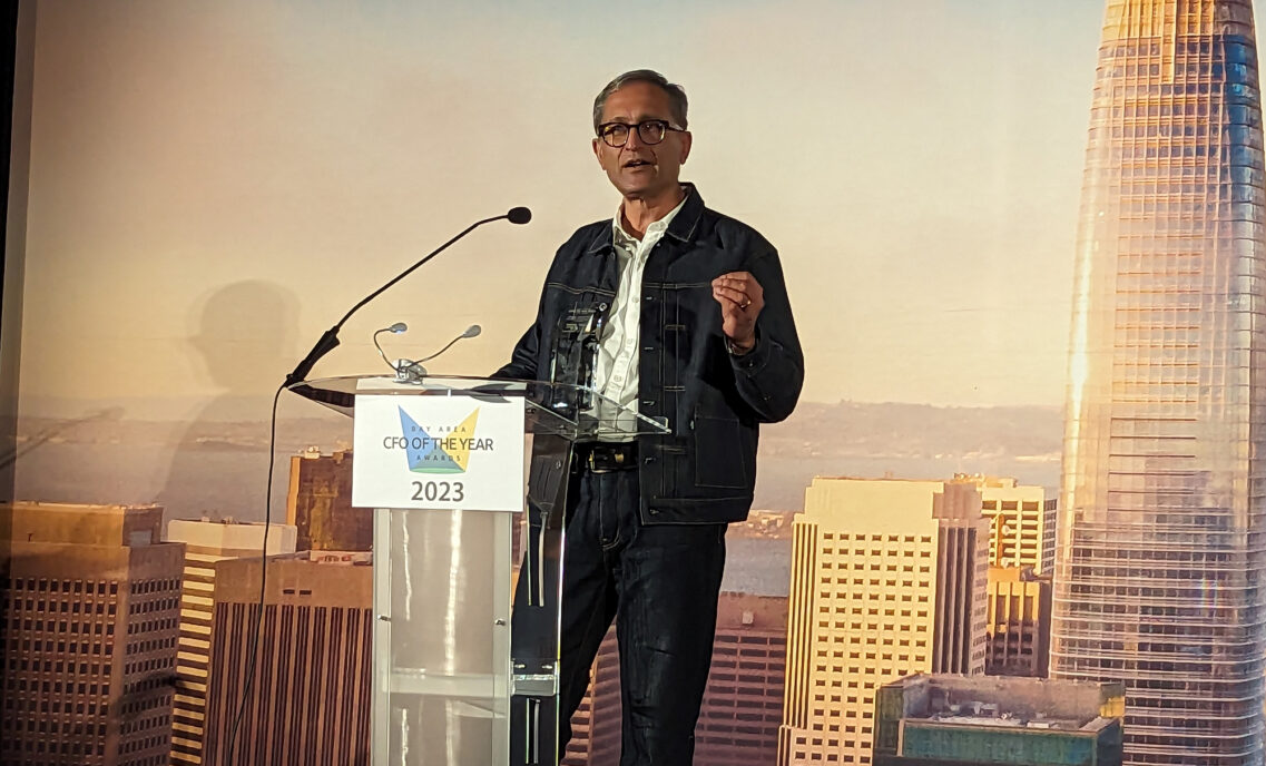 LS&Co. Chief Financial & Growth Officer Harmit Singh stands at a podium with a San Francisco skyline backdrop to accept the Larkin Street 2023 Hall of Fame Lifetime Achievement Award.