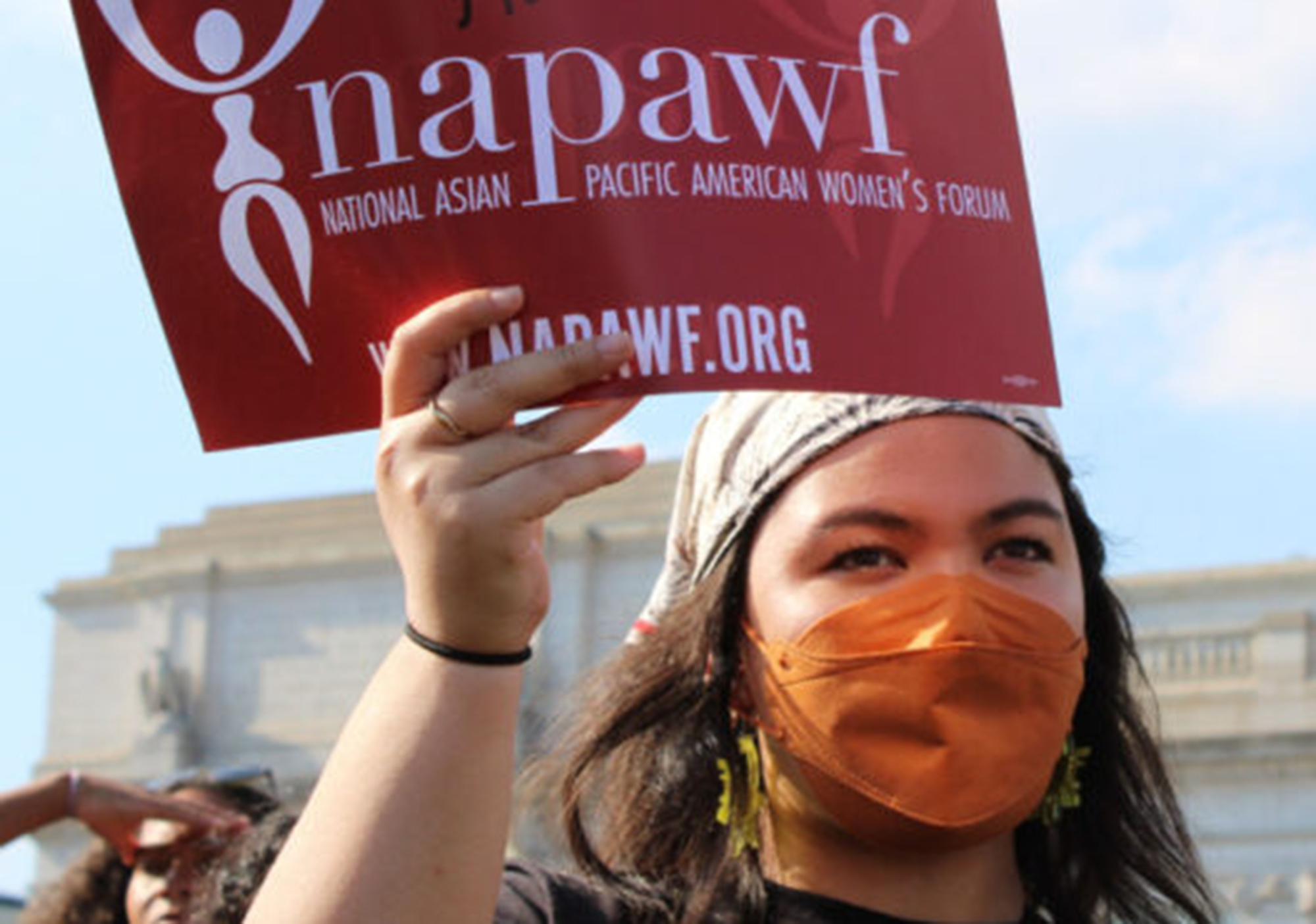 A person holds a red sign with their right hand that reads 