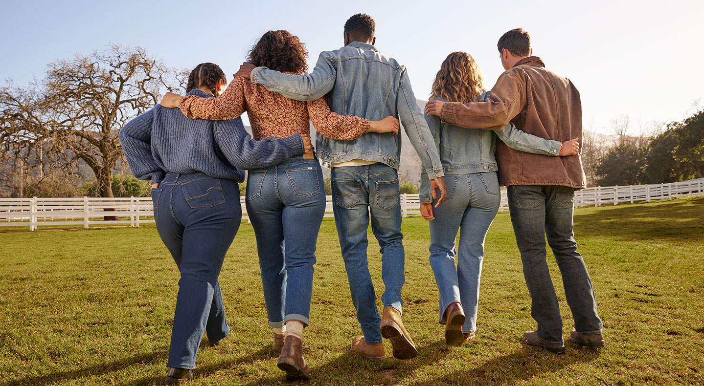 Five people link arms and face away from the camera, wearing Signature by Levi Strauss clothing. They are standing on grass. Photographer: Sara Byrne + Phil Chester