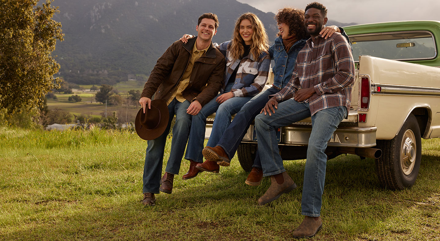A group of four people sit on the back of a pickup truck in a grass field. They wear Signature by Levi Strauss & Co. clothing and western themed outfits. Photographer: Sara Byrne + Phil Chester
