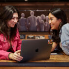 Two LS&Co. employees sit at a table with a laptop in between them. The person on the right is wearing a pink Levi's® jacket and the person on the right is wearing a denim jacket.