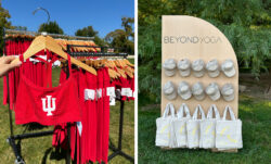 Left: a hand holds a red Beyond Yoga® sports bra labeled with a university logo. Right: a display of tan Beyond Yoga® hats and canvas tote bags hang on a wooden peg board.