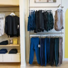 An assortment of athleisure products hang on clothes racks and are stacked in the interior of a Beyond Yoga® store. A yellow sign hangs on the right reading "Get to Know Us. Female founded and led since 2005. Universally flattering, inclusive sizes: XXS-4X. Join our community @BeyondYoga. Made to last for years to come"