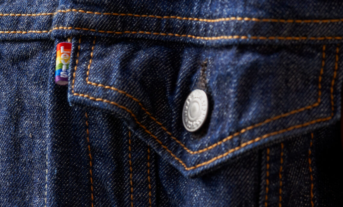 A zoomed in image of a Levi's® dark wash denim jacket, featuring a rainbow Levi's® pride tab next to the front pocket.