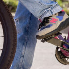 A cropped-in photo of a person's legs pedaling a bike. They are wearing denim jeans and the new Levi's® x New Balance MT580 shoe.