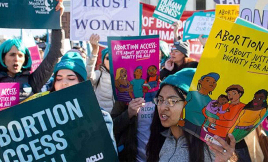 People gather holding signs advocating for reproductive rights and abortion access.