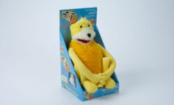 "Flat Eric," a yellow plush puppet, sits packaged in a box. 