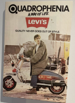 A movie poster for the 1979 film “Quadrophenia.” Protagonist Jimmy Cooper sits on a red scooter with his hands on the handlebar wearing a military fishtail parka and Levi's® 501® jeans. He is looking off towards the right. Text on the top of the poster reads in all caps: "Quadrophenia" followed by "a way of life" and the red Levi's® batwing logo. the text "quality never goes out of style" is under the logo.