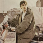 Protagonist character Jimmy Cooper sits on a red scooter with his hands on the handlebar in the 1979 film “Quadrophenia,” wearing a military fishtail parka and looking off towards the right.