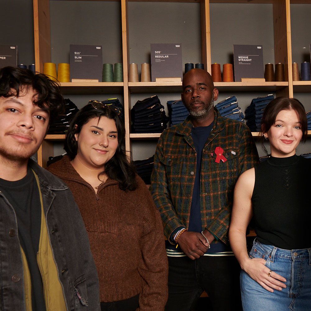 Four retail employees smile in front of a wall of Levi's® product at the Levi's® San Francisco Market Street store.