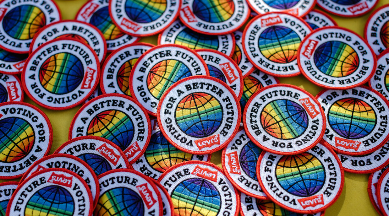 A pile of Levi's® patches that feature a red border with a rainbow colored circle design in the middle and the words "voting for a better future" around the center, as well as a red Levi's® batwing logo at the bottom center.