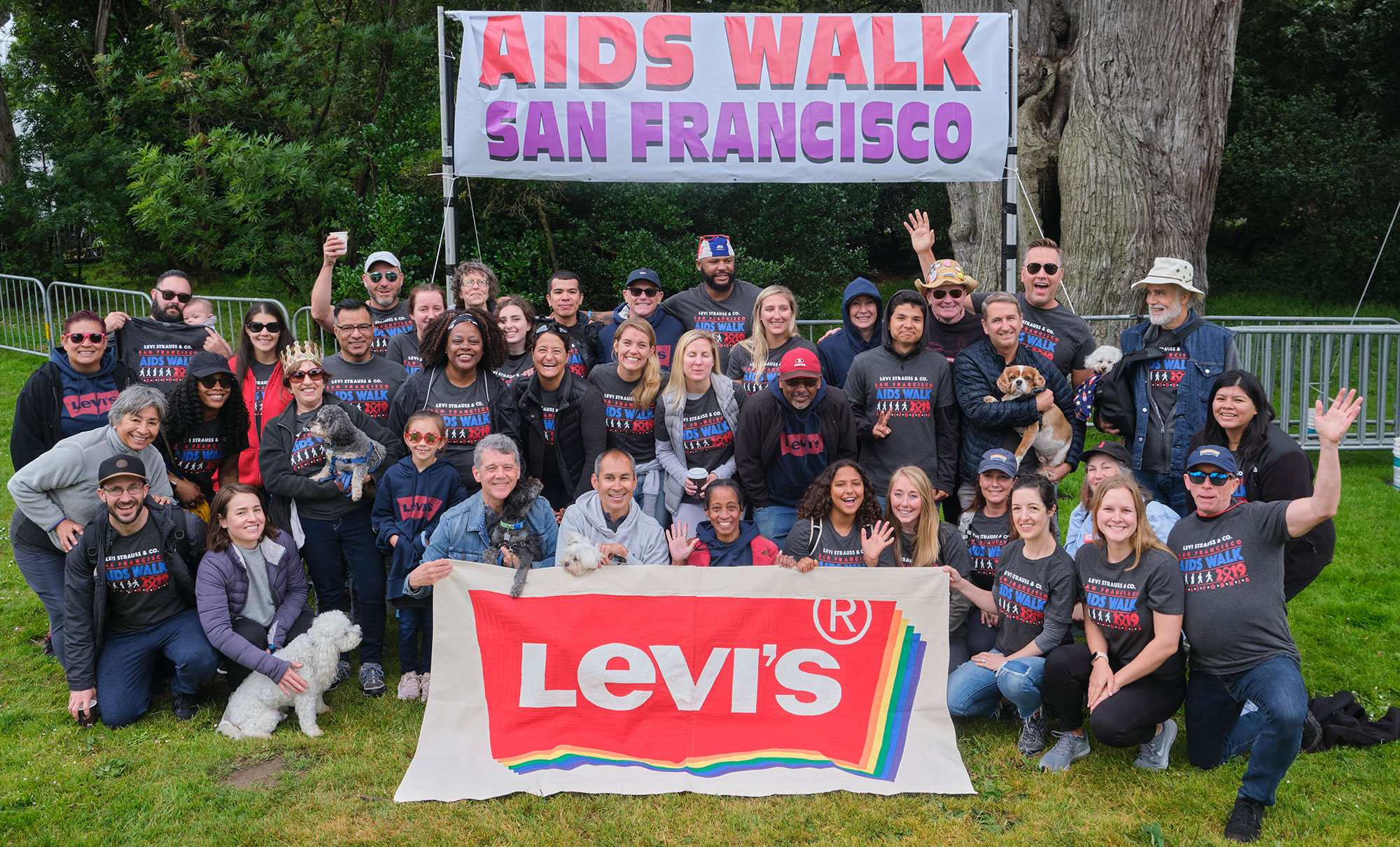 A large group of LS&Co. employee volunteers pose in matching Aids Walk 2019 shirts in front of a sign reading "Aids Walk San Francisco." In front of them is a large sign of the Levi's® pride logo with rainbow coloring.