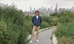 A person stands on a path in a park wearing a Levi's® blue denim jacket and beige Levi's® 511 Tech pants. Their hands are in their pockets. A city skyline can be seen behind them in the distance.