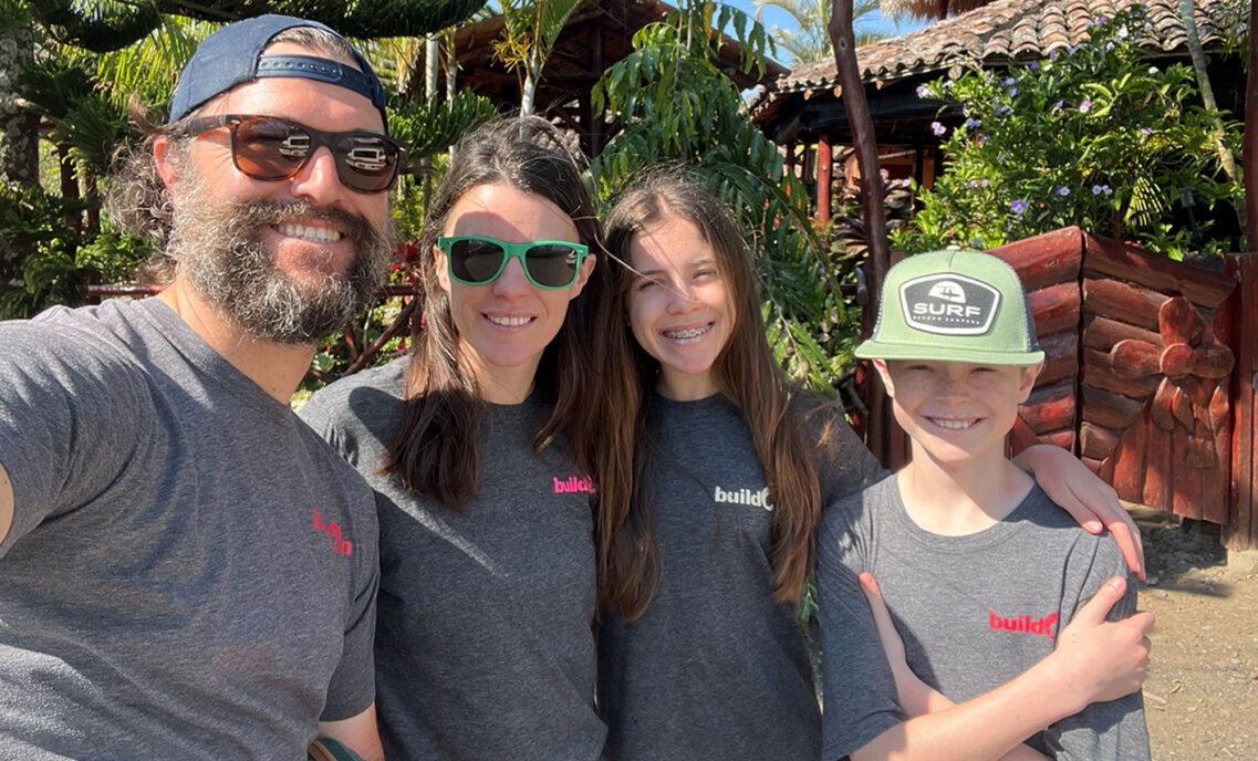 Orla Hollub, VP, global head of finance and strategy at Dockers®, smiles with her husband and two children. They are all wearing matching grey long sleeve shirts with the word "build" on the right pocket.