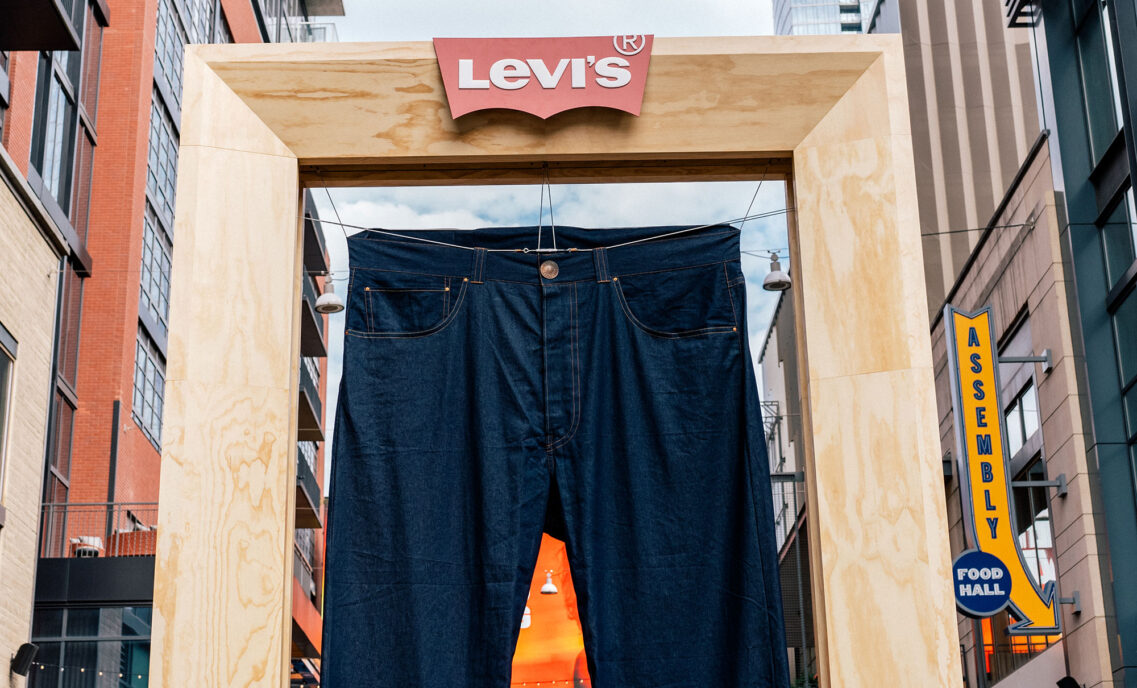 A pair of giant Levi's® 501® jeans hangs in a wooden frame with the red Levi's® batwing logo at the top.