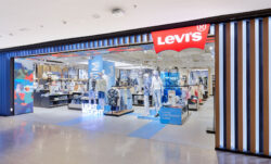 The front entrance of the Levi's® CentralWorld store in Bangkok, Thailand, featuring wooden slats on the right and a red Levi's® batwing logo on the top of the open storefront. Various product displays can be seen on the store floor inside.
