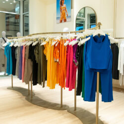 A colorful array of Beyond Yoga® products hang on a display rack inside the Beyond Yoga® Bellevue store. A blue tank and leggings can be seen at the front of the rack, followed by sets in pink, orange, purple, grey and turquoise hues.
