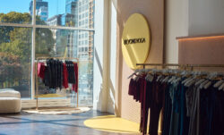 Two racks of Beyond Yoga® clothing and a yellow circular sign reading Beyond Yoga in the Beyond Yoga® Club Beyond pop-up