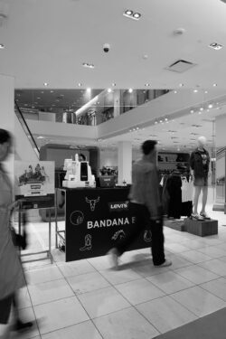 A black and white image of a Levi's® pop-up experience in a Holt Renfrew department store, featuring people walking by a bandana customization booth with Levi's branding