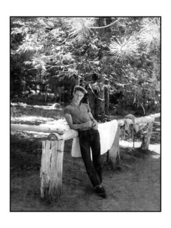 A black and white image of Levi's® fan Robert Brecko as a teenager in 1954 at a camping trip in Pinecrest. He leans on a log fence wearing a cap, shirt and Levi's® 501® jeans.