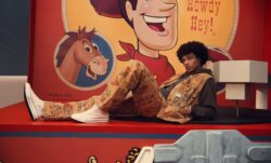A person lays on a red bench against Toy Story graphics. They wear a matching Toy Story patterned Levi's® vest and pants