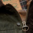 A close up image of the Levi’s® x Barbour Spey Wax Jacket, which reimagines Barbour’s classic silhouette in tobacco wax with brown cord collar, featuring pocket flaps shaped like Levi’s® iconic arcuate, trucker-style cuffs and waistband, and a back-cinch characteristic of Levi’s® archival denim. With moleskin pocket lining and co-branded elements throughout, the piece bridges outdoor functionality with authentic Western workwear DNA.