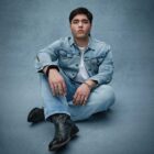 Folk singer‑songwriter Kevin Kaarl poses in a Levi's® denim jacket, Levi's® jeans and black boots against a blue background for the Levi’s® and COLORSxSTUDIOS global music program, EMERGENT.