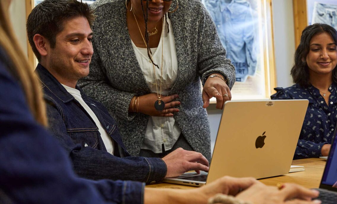A Levi Strauss & Co. employee sits at a table looking at their laptop as another employee points to their screen