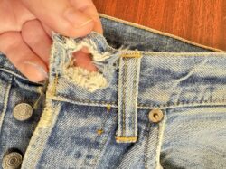 A person's fingers hold open a frayed buttonhole on a pair of Levi's® 501® jeans 