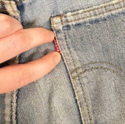 Two fingers point to a red Tab on the back pocket of a light wash pair of Bruce Springsteen's Levi's® 501® jeans 