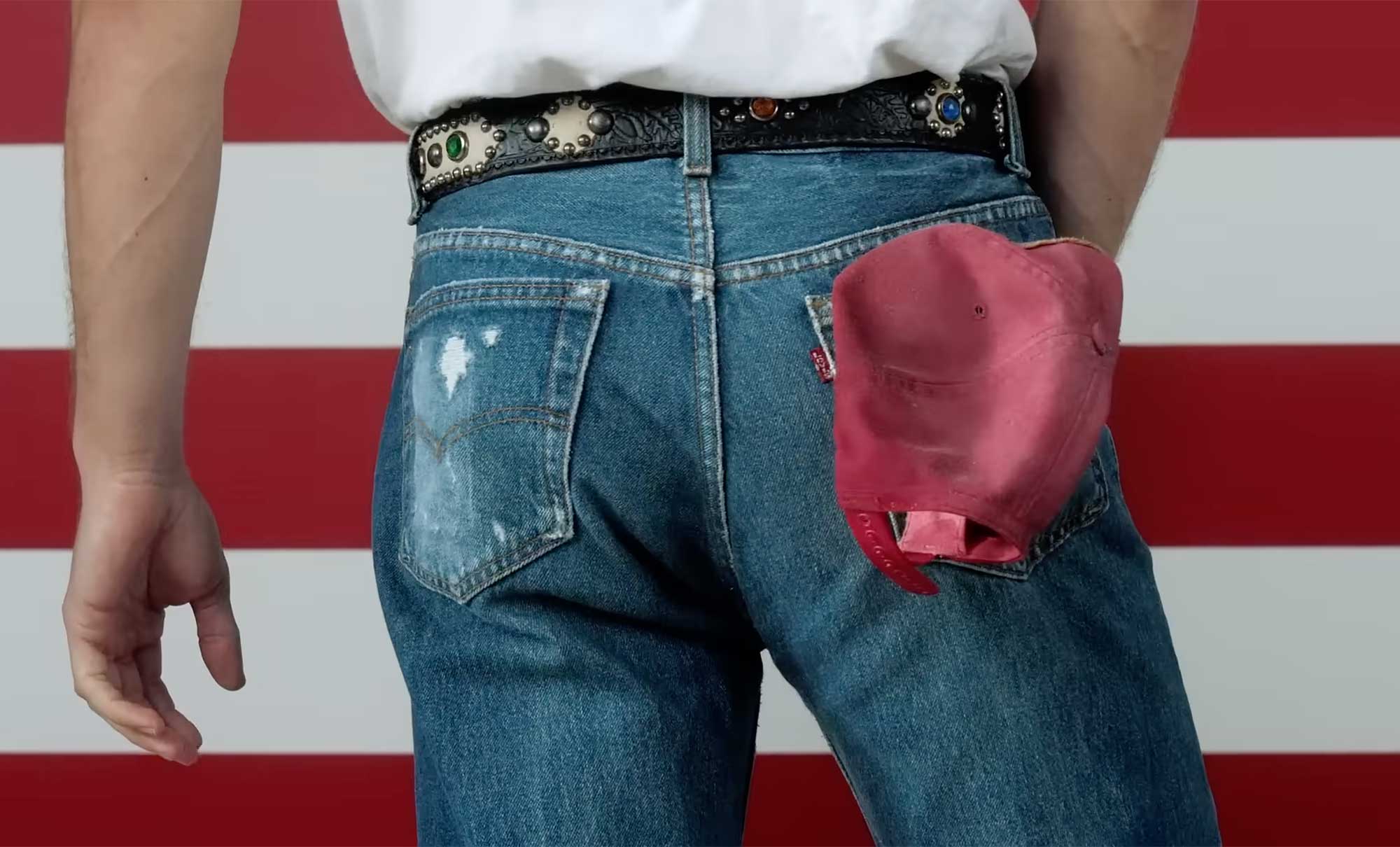 A recreation of Bruce Springsteen's “Born in the U.S.A.” album, featuring a backside wearing Levi's® 501® jeans, a black studded belt, white t-shirt, and red baseball cap in the back right pocket against red and white stripes.